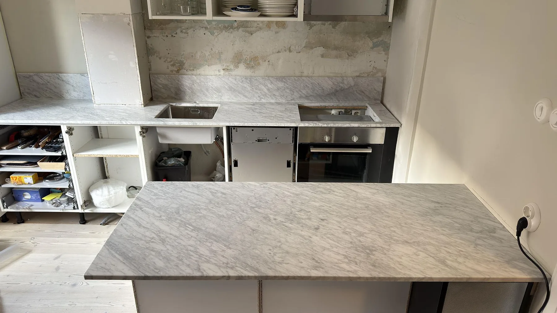 Köksbänkskiva och stor köksö i matt Carrara C marmor, 20 mm, med låg stänkkant, rostfri diskho och hällurtag i ett kök i Solna.