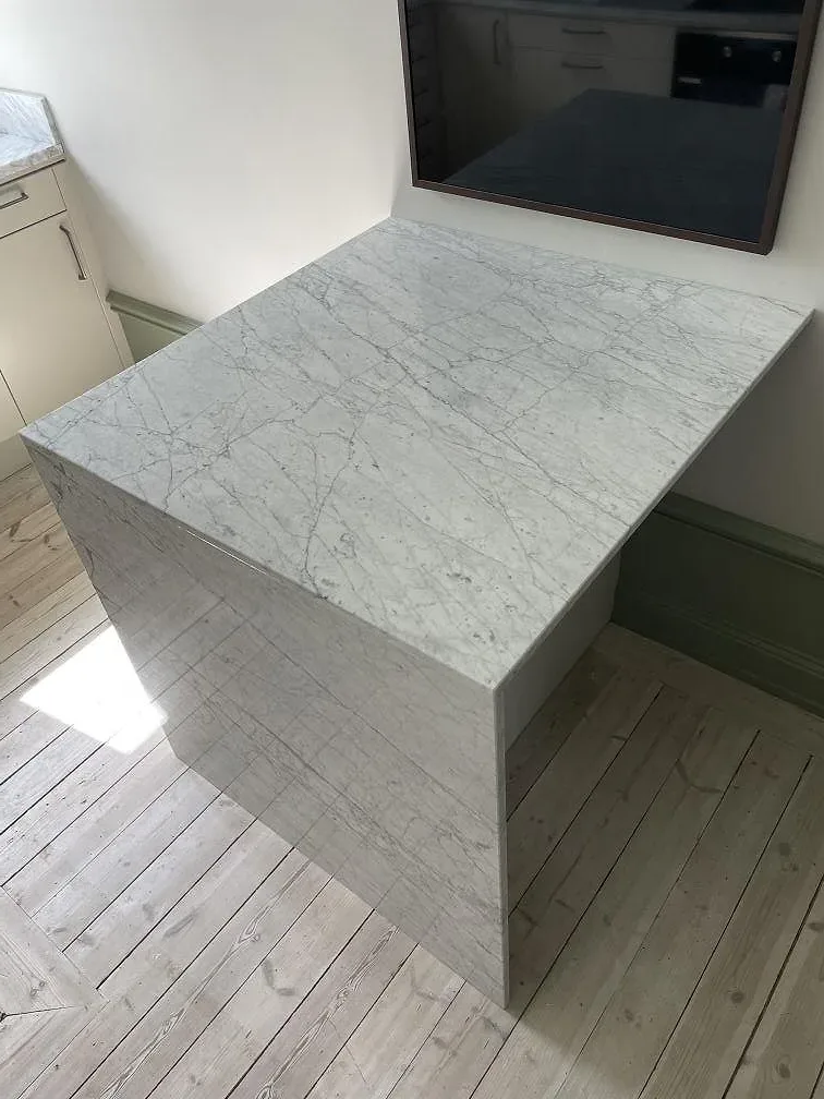 Frihängande köksö i vit Carrara C marmor, 20 mm polerad, med nedfälld sidokant mot ljust trägolv i ett kök i Solna.