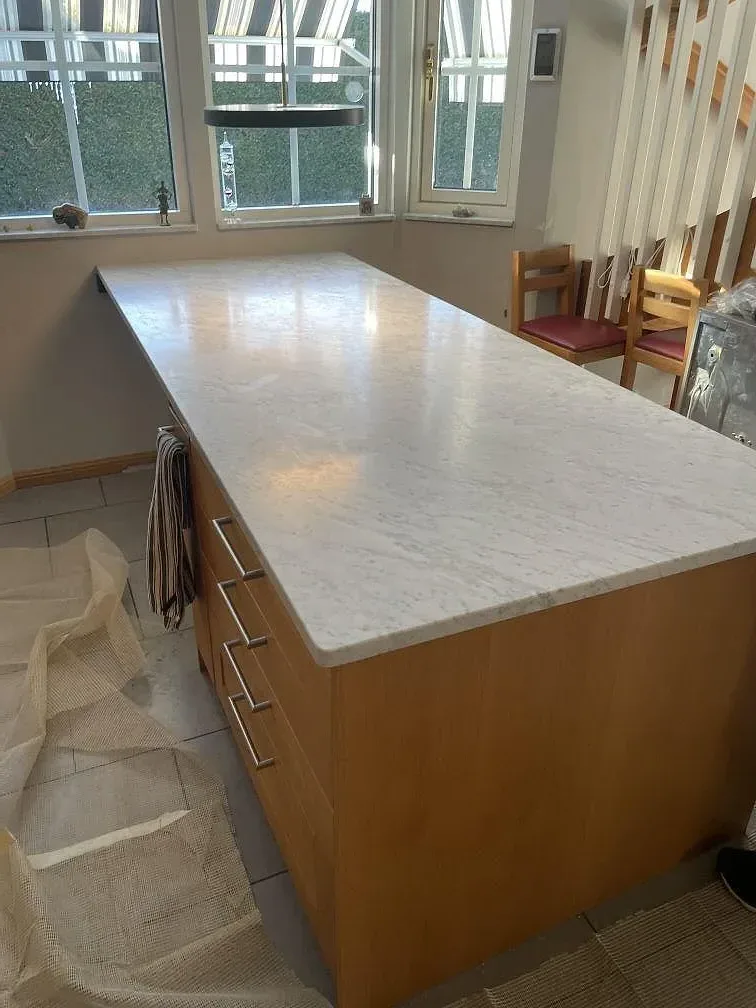 Köksö i Carrara C-marmor med ekvattenfall fotograferad mot fönstret i ett kök under montering i Spånga.