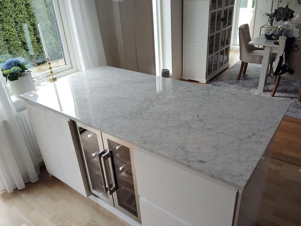Köksö med bänkskiva i polerad Carrara C marmor, 30 mm, över vita skåp och vinkyl i ett kök i Spånga.
