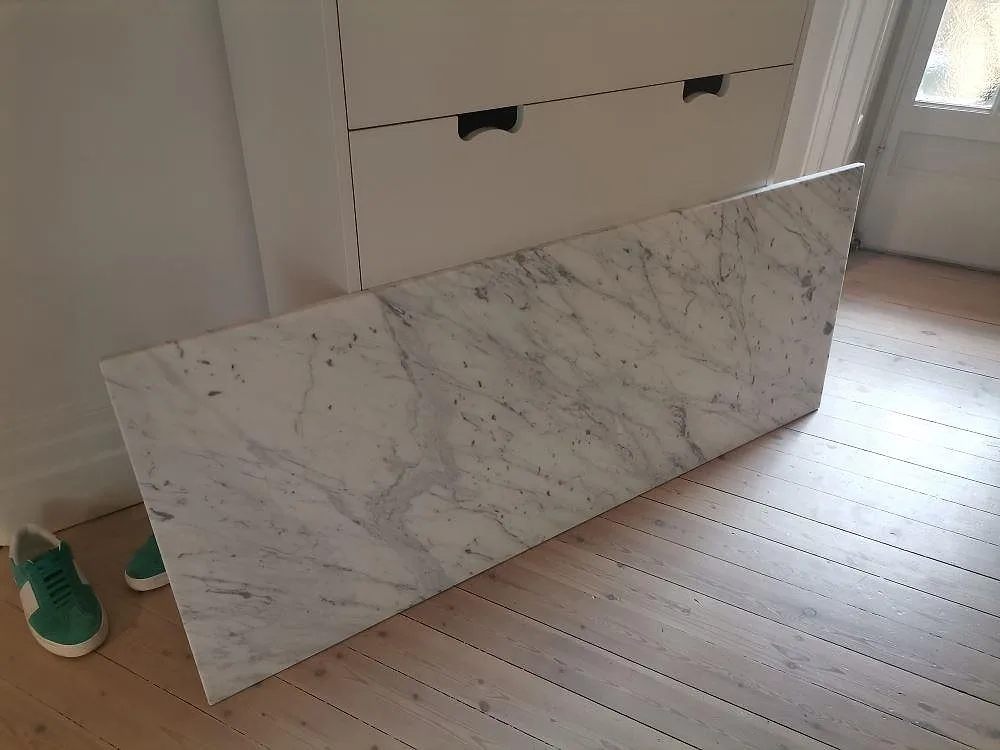 Måttkapad bänkskiva i vit Carraramarmor Carrara C med tydlig grå ådring, lutad inomhus inför montering i Stockholm.