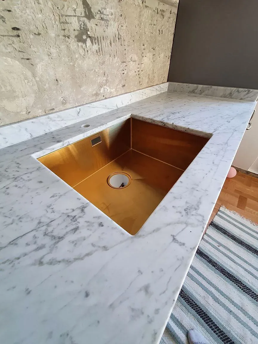 Köksbänkskiva i matt Carrara C marmor med infälld diskho och häll i ett kök i Stockholm.