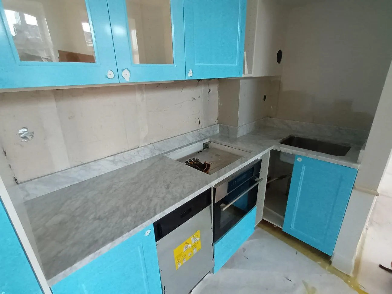 Köksbänkskiva i polerad Carrara C-marmor med uppvikt stenkant och synliga urtag i ett kök under montering i Stockholm.