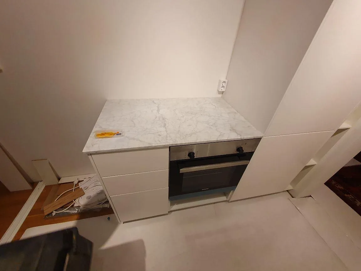 Matt Carrara C marmorbänkskiva över vita köksstommar och ugnssektion i ett kök under montering i Stockholm.