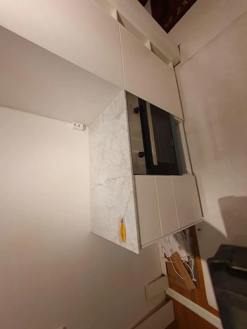Bänkskiva i Carrara C marmor, matt, med inbyggd ugn och underliggande lådhurts i ett kök under montering i Stockholm.