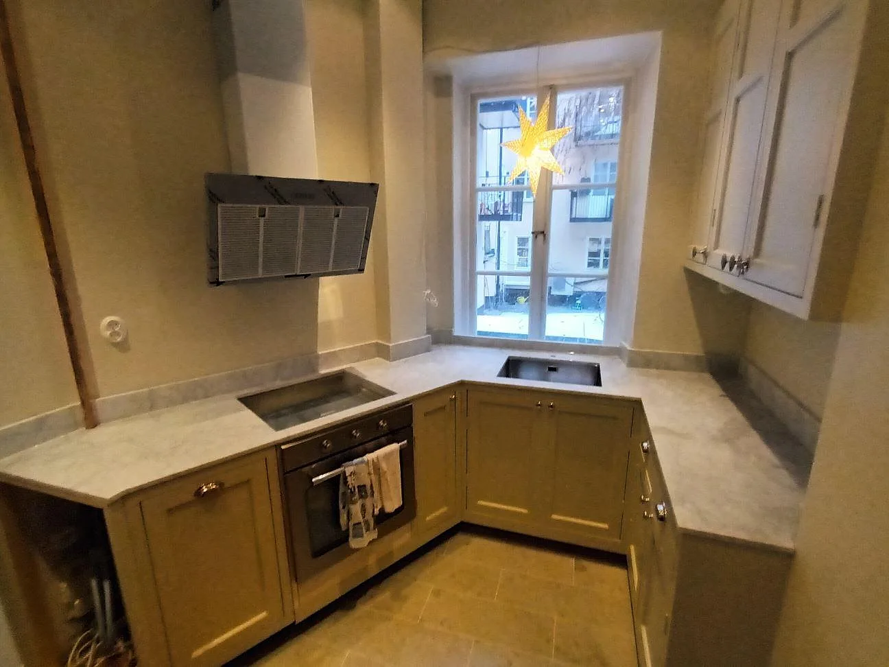 Köksbänkskiva i matt Carrara C-marmor med grå ådring, induktionshäll och underlimmad diskho i ett U-format kök i Stockholm.