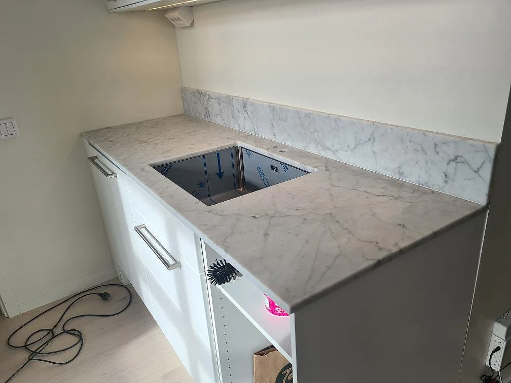 Matt Carrara C marmorbänkskiva med underlimmad rostfri diskho och uppvikt stänkkant i ett U-format kök i Stockholm.