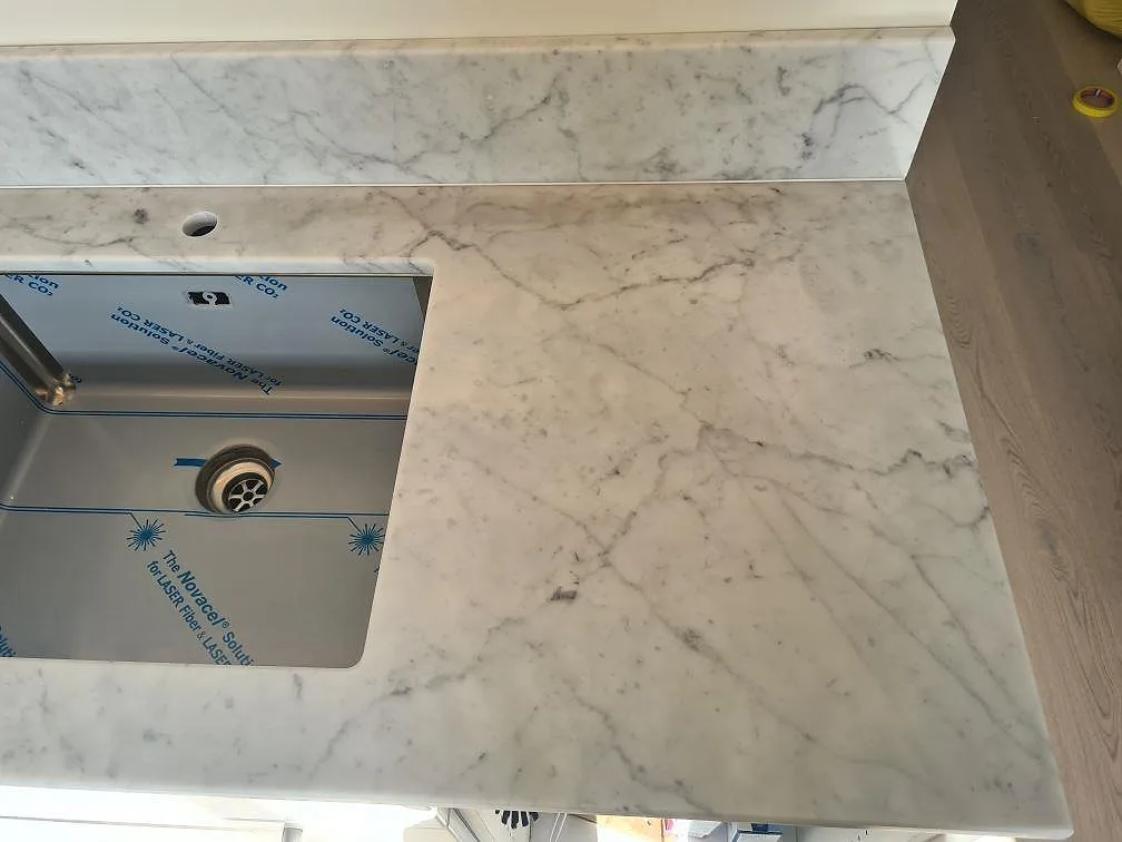 Närbild av Carrara C marmor kring underlimmad rostfri diskho och ljus köksbänk i Stockholm.