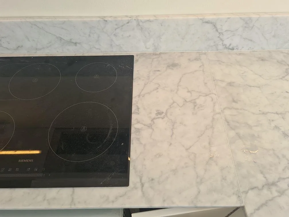 Carrara C köksbänkskiva i matt marmor med svart induktionshäll, skarv och uppvikt stänkkant i Stockholm.