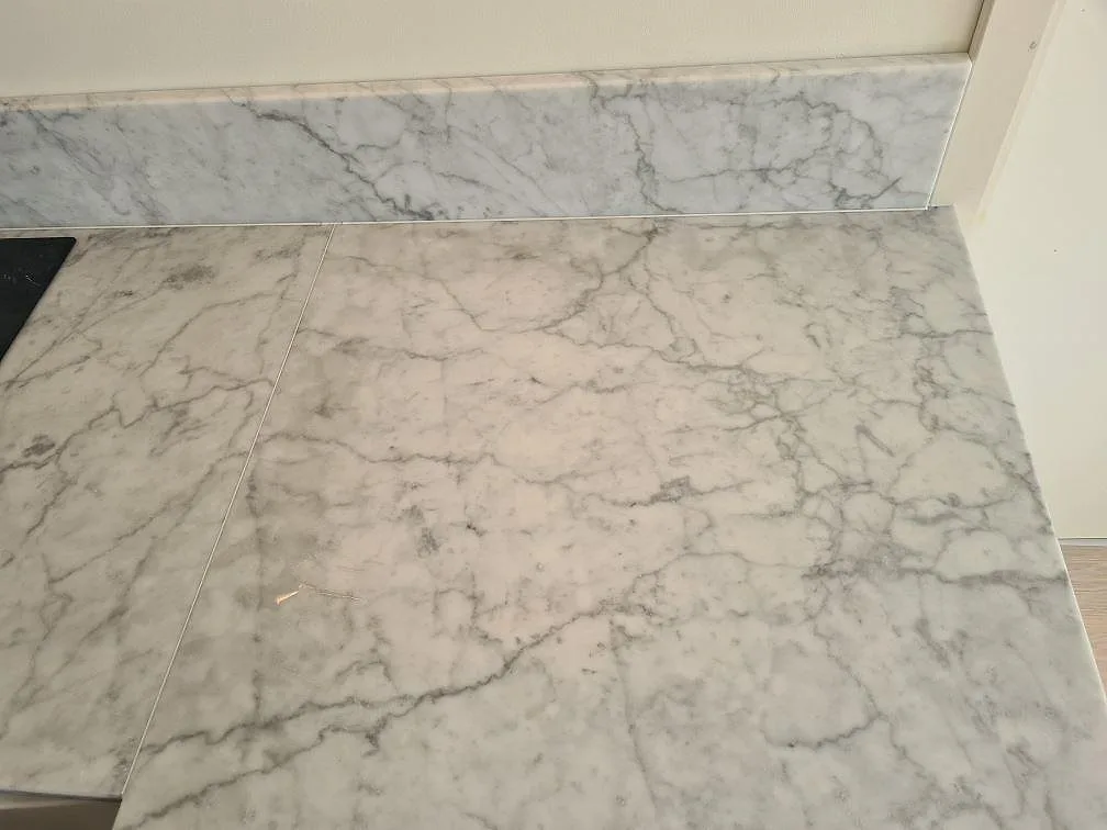 Arbetsyta i matt Carrara C marmor med tydlig grå ådring och stänkkant intill häll i Stockholm.