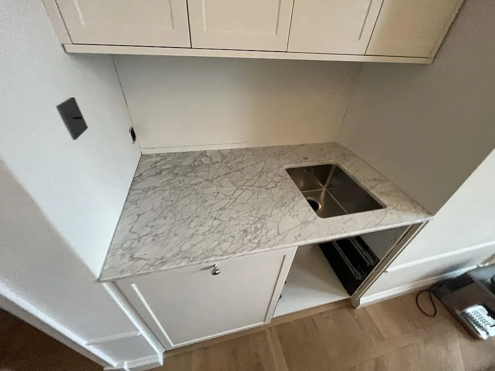 Bänkskiva i matt Carrara C marmor med underlimmad diskho och vit köksinredning under montering i Stockholm.