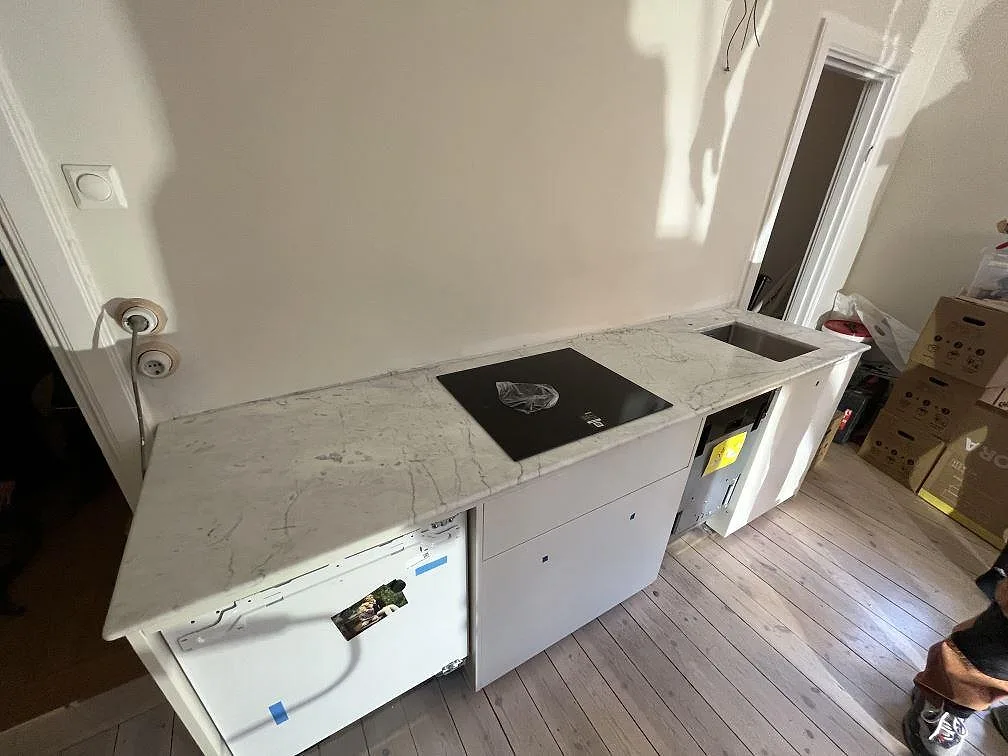 Matt köksbänkskiva i Carrara C-marmor med häll på vita köksskåp under montering i Stockholm.