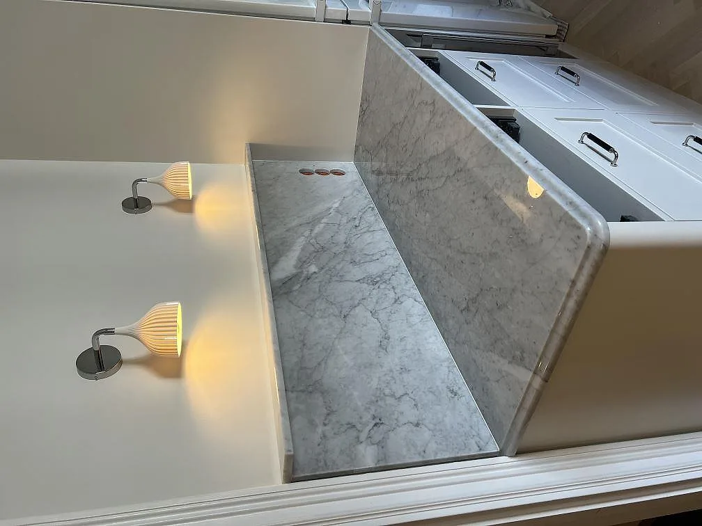 Polerad Carrara C marmor som topp och sidostycke i en LED-belyst nisch intill shakerluckor i Stockholm.