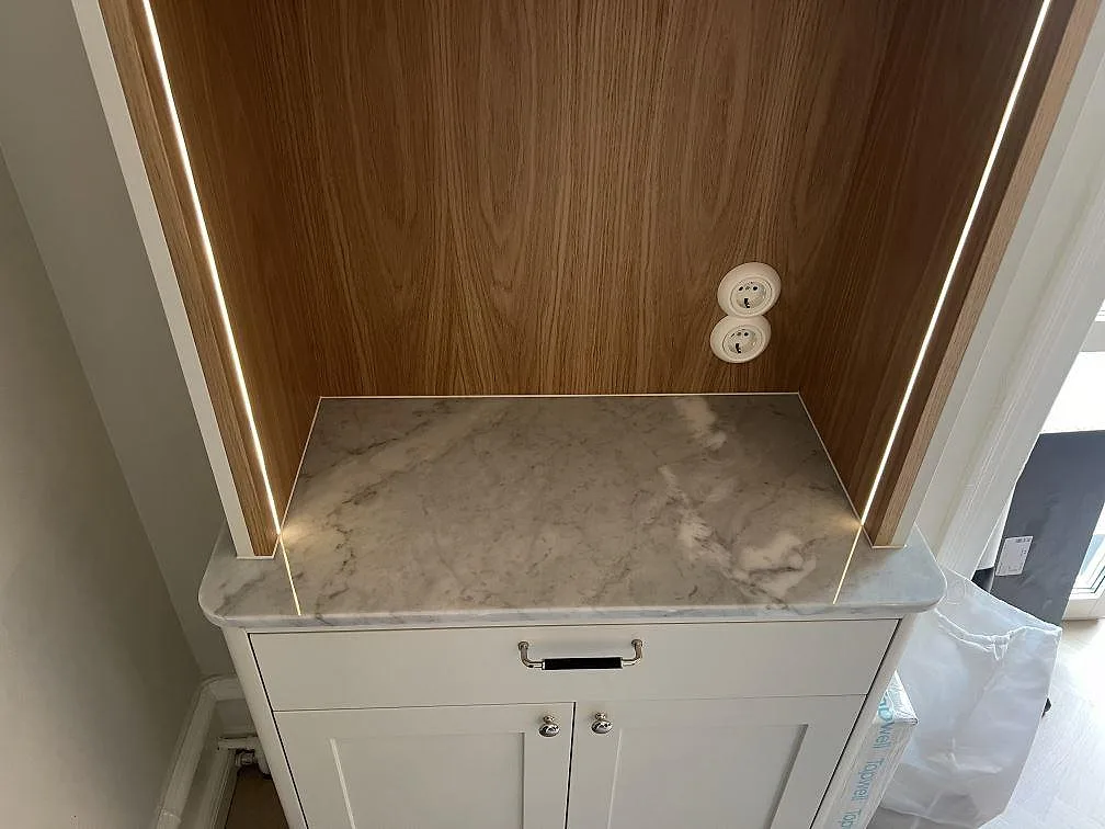 Separat skåp med polerad Carrara C marmortopp, rundade framhörn och LED-belyst träfond i Stockholm.