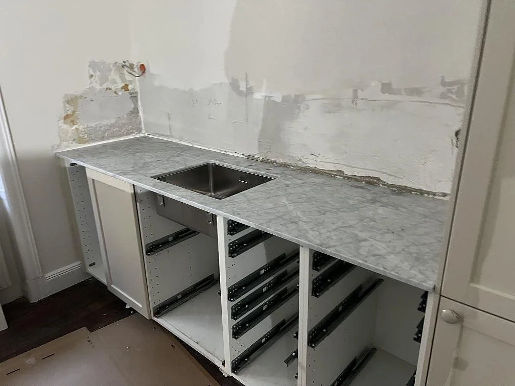 Rak köksbänkskiva i matt Carrara C-marmor, 20 mm, med synlig diskho och grå ådring i ett kök i Stockholm.