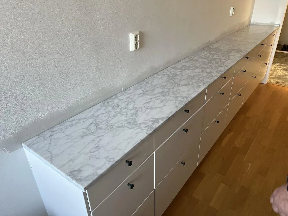 Lång köksbänkskiva i matt Carrara C marmor med sammanhållen ådring längs en skåprad i Stockholm.