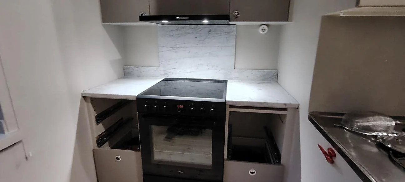 Matt Carrara C marmor som köksbänkskiva och stänkskydd bakom fristående spis i ett kök under montering i Stockholm.