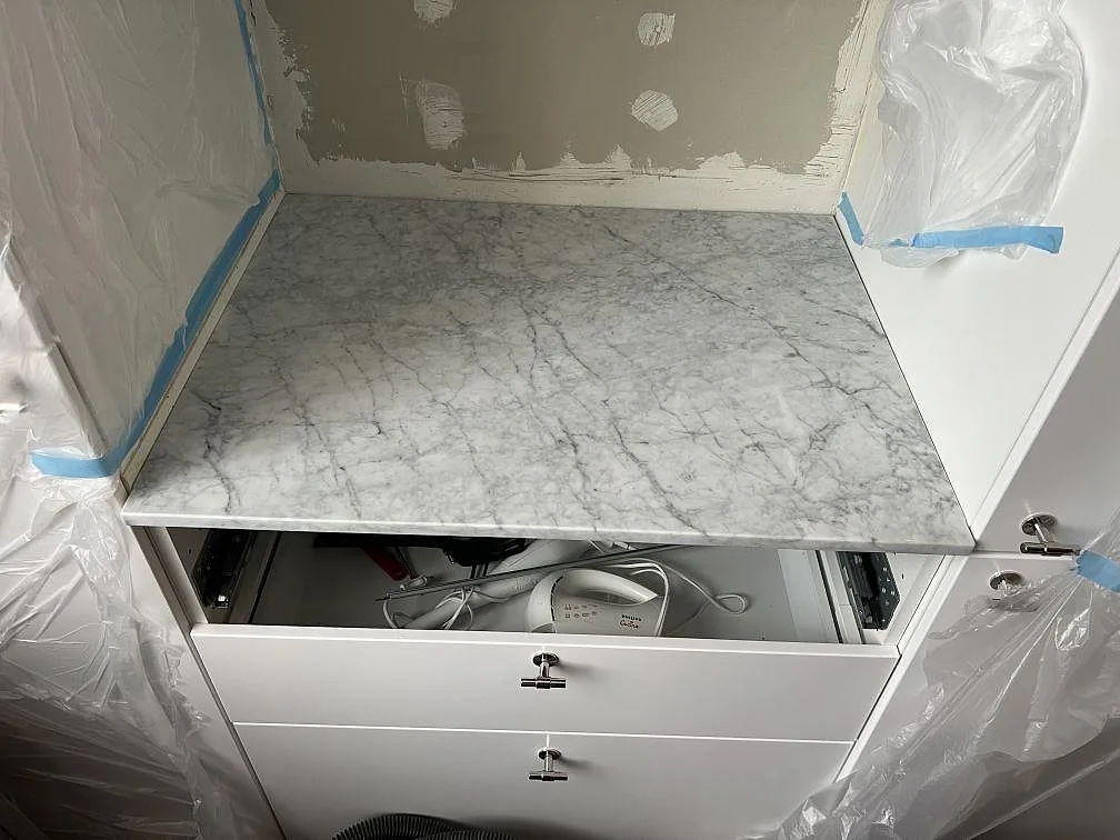 Mindre bänkskiva i matt Carrara C-marmor med grå ådring på ett skåp under montering i Stockholm.