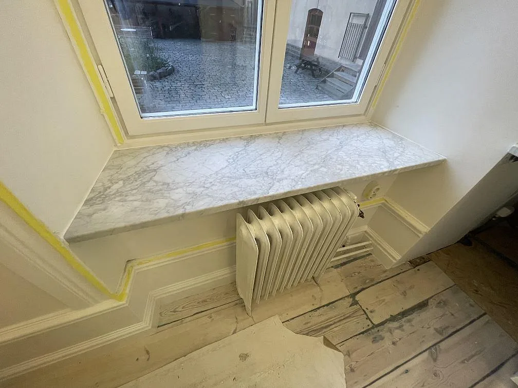 Fönsterbänk i Carrara C marmor, 30 mm matt, med grå ådring ovanför radiator vid ett fönster i Stockholm.