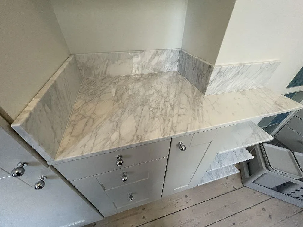 Polerad Carrara C marmor som bänkskiva och uppvikt stänkskydd runt en nisch i ett kompakt kök i Stockholm.