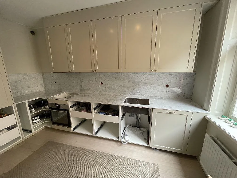 Närbild av polerad Carrara C-marmor som bänkskiva och stänkskydd längs vit köksinredning under montering i Stockholm.
