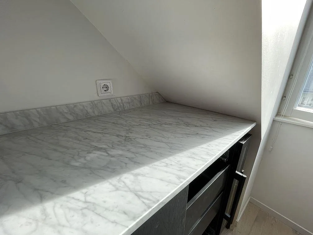 Närbild av matt Carrara C marmor med grå ådring, låg stänkkant och fri arbetsyta vid fönster i Stockholm.
