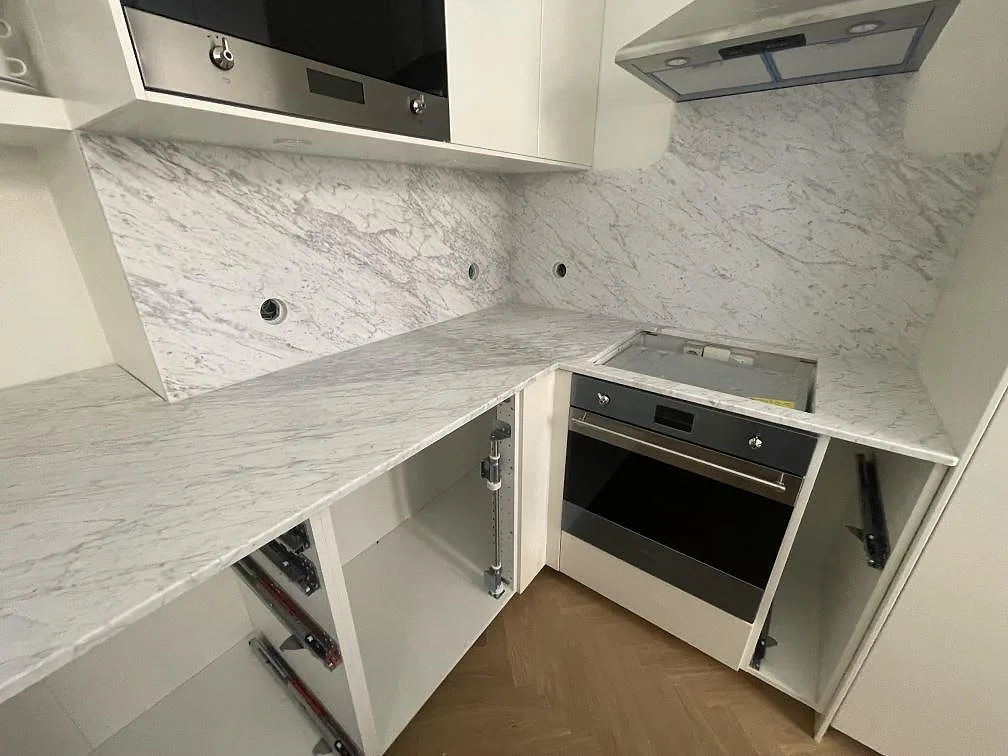 L-formad köksbänkskiva i matt Carrara C-marmor med stänkskydd och spiszon i Stockholm.
