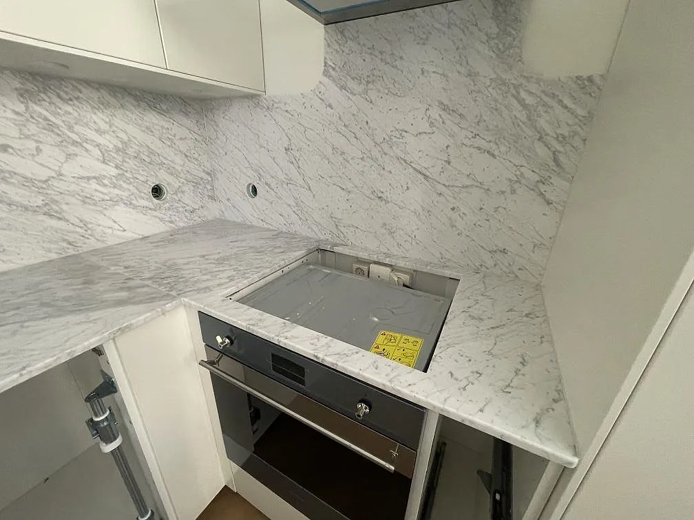 Närbild på matt Carrara C-marmor som köksbänkskiva med öppning vid spis och marmorklädd vägg i Stockholm.