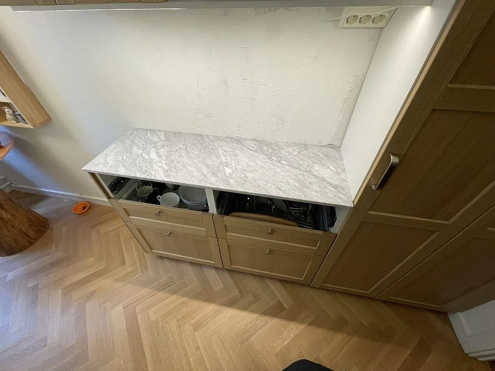 Rak bänkskiva i matt Carrara C marmor, 20 mm, på trästommar vid högskåp i Stockholm.