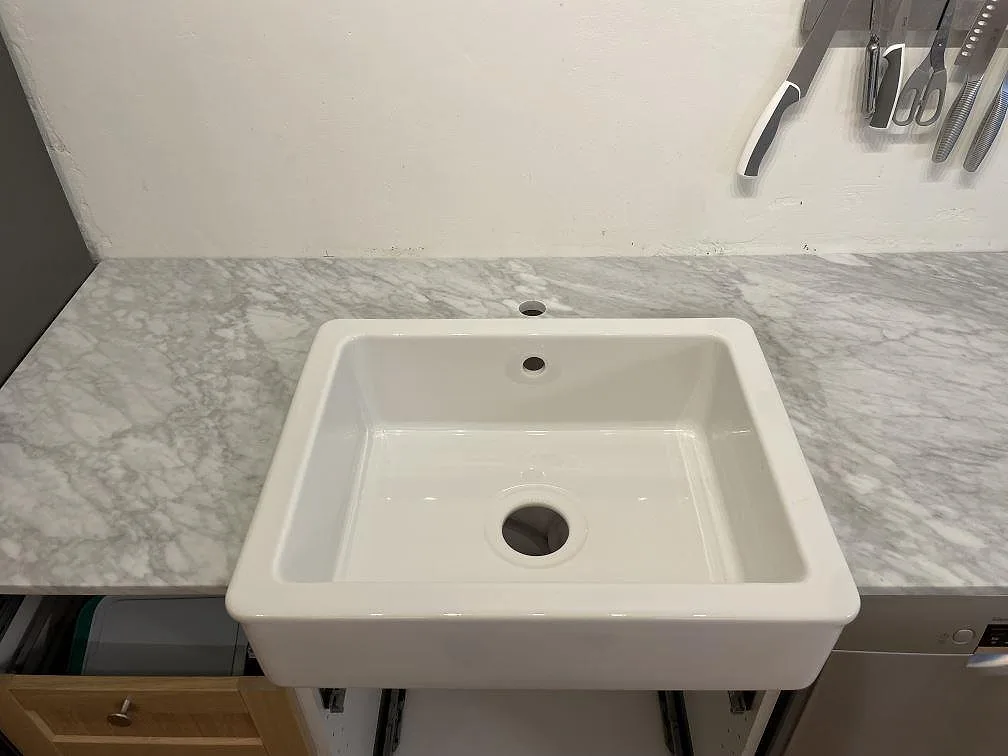 Närbild på matt Carrara C marmor runt en vit diskho i ett kök under montering i Stockholm.