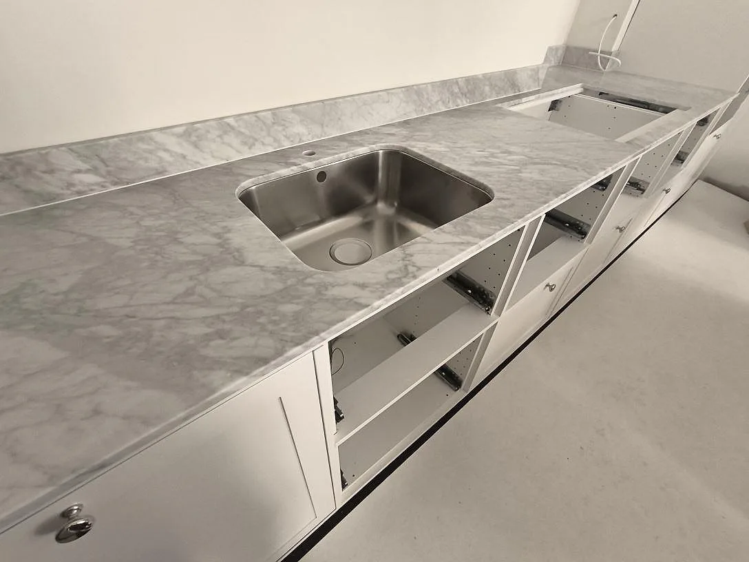 Närbild på matt Carrara C marmor med grå ådring, rostfri diskho och öppen vit köksstomme i Stockholm.