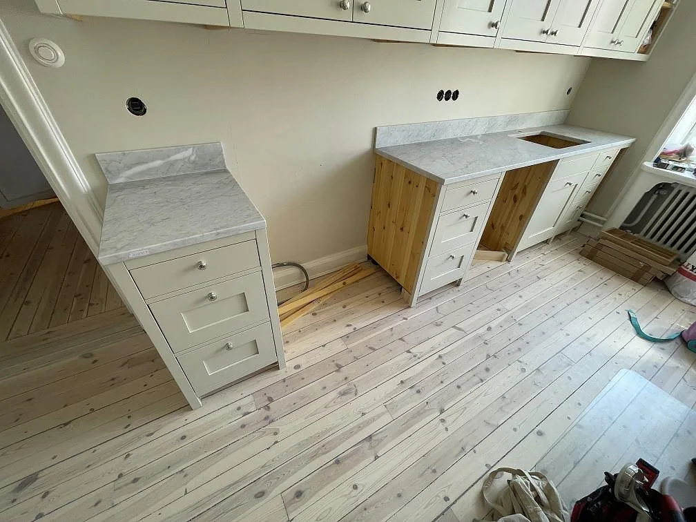 Köksbänkskiva i matt Carrara C marmor med låg stänkkant och ljusa köksstommar under montering i Stockholm.