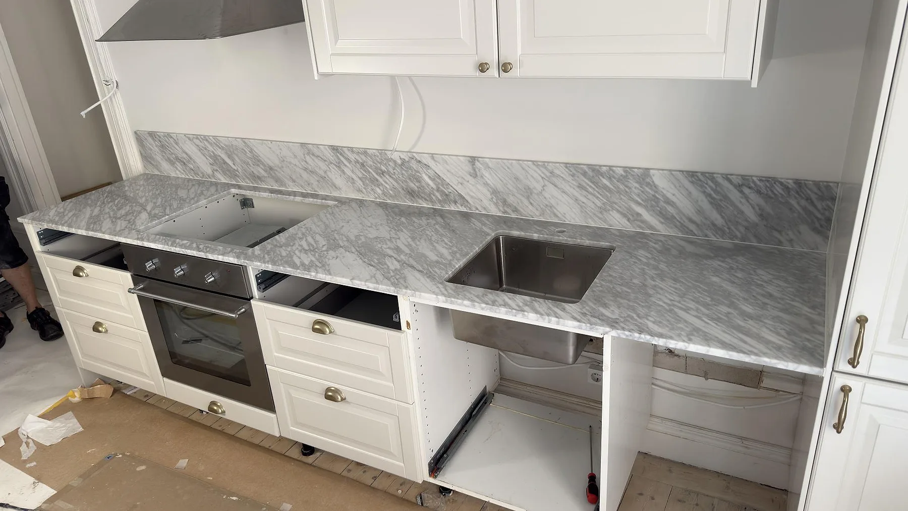 Matt bänkskiva i Carrara C-marmor med grå ådring, stänkkant och arbetsyta under montering i Stockholm.