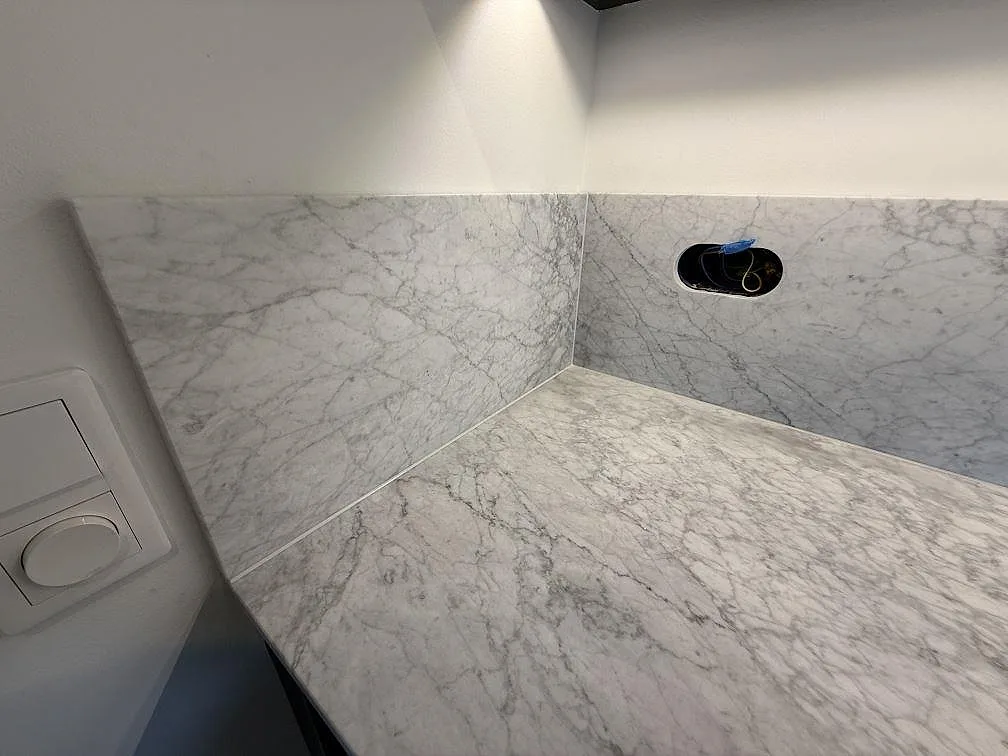 Närbild på matt Carrara C marmor som bänkskiva och uppvikt stänkskydd i kök i Stockholm.
