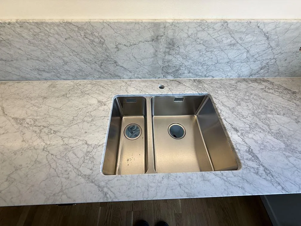 Köksbänkskiva i matt Carrara C marmor med rostfri diskho och stänkskydd i Stockholm.
