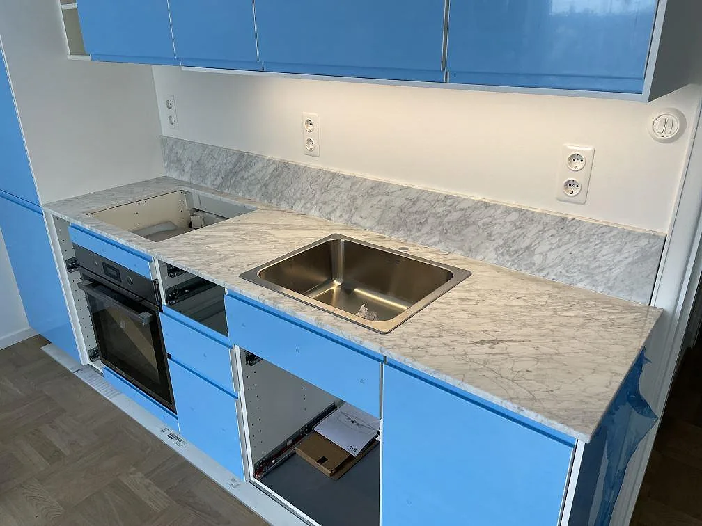Polerad Carrara C marmorbänkskiva med tät grå ådring, låg stänkkant och lång arbetsyta i ett kök under montering i Stockholm.