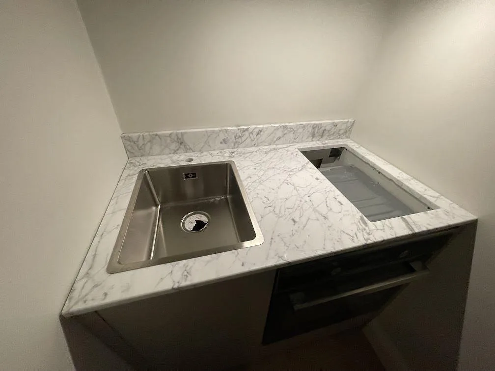 Polerad marmorbänkskiva i Carrara C med synlig ådring, rostfri diskho och hällurtag i ett kök i Stockholm.