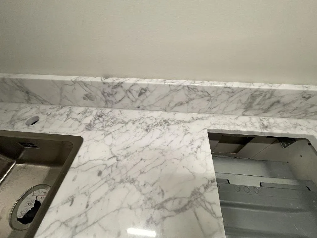 Detalj av polerad Carrara C bänkskiva med grå ådring, uppvikt stänkskydd, diskho och hällurtag i Stockholm.