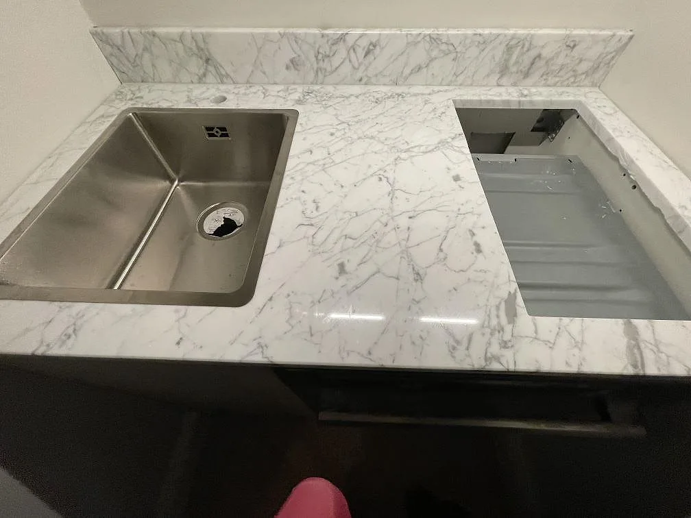 Närbild av köksbänkskiva i polerad Carrara C marmor med diskho, hällurtag och blank ådrad yta i Stockholm.
