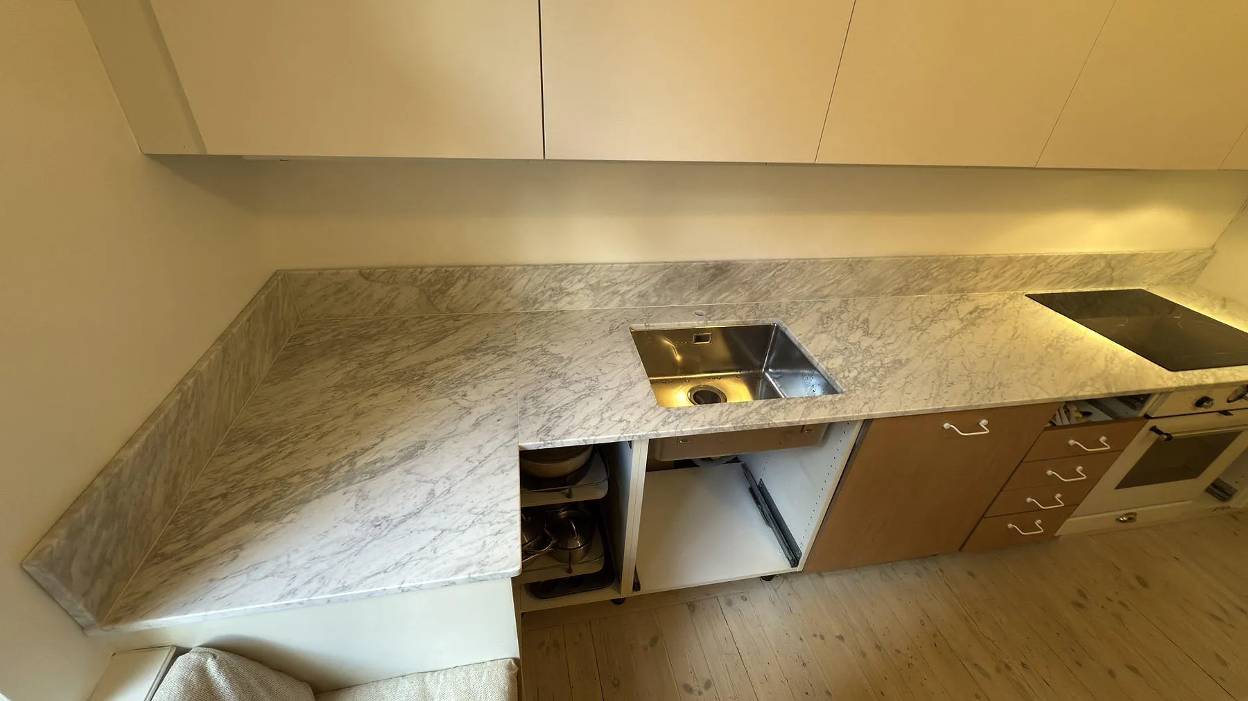 Närmare vy över Carrara C marmor i 20 mm matt finish med rostfri diskho och låg stänkkant längs fönsternischen i ett stockholmskök.