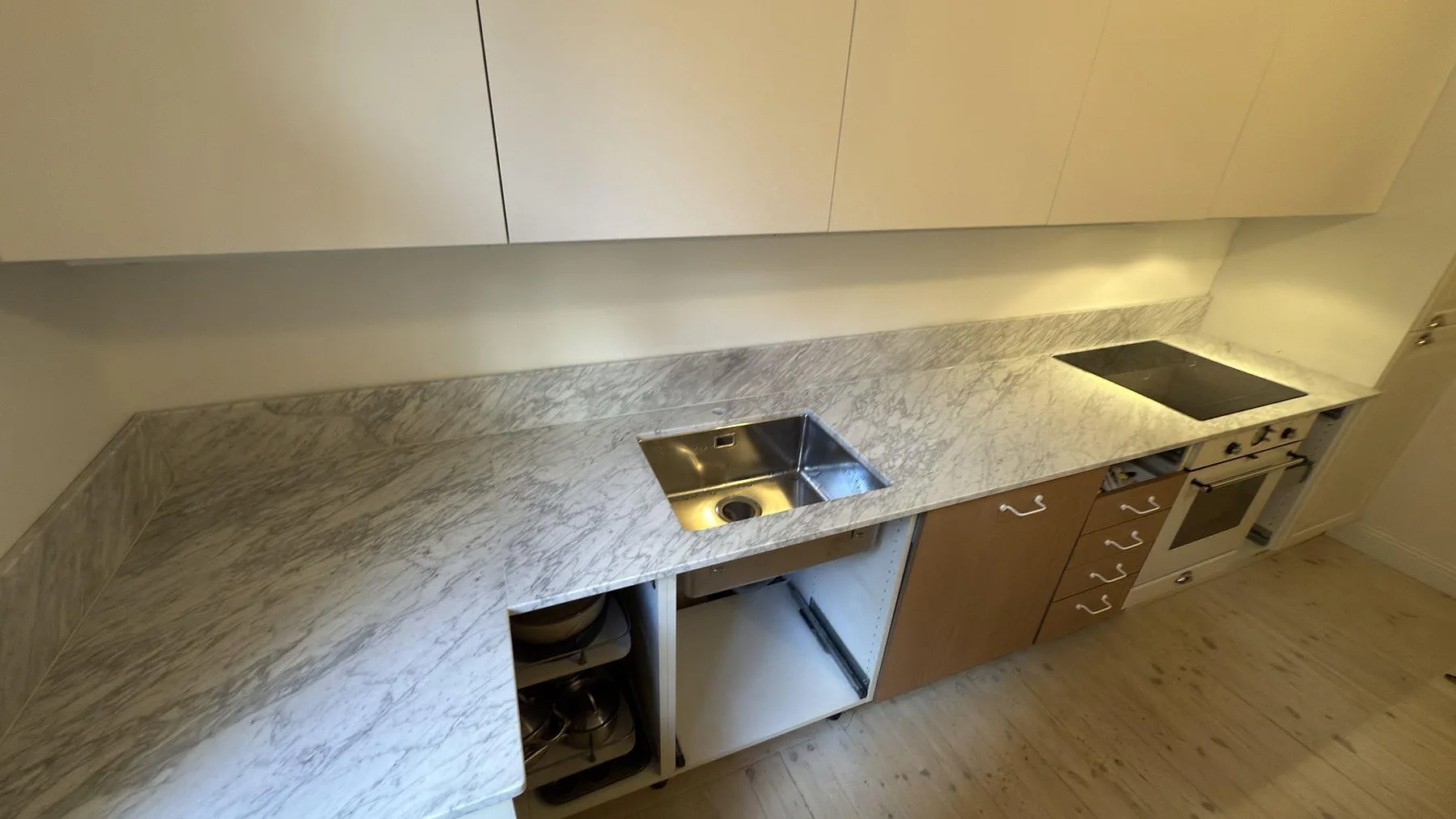 Matt Carrara C marmor som väggmonterad köksbänk med underlimmad rostfri diskho, låg stänkkant och häll vid högerkant i Stockholm.
