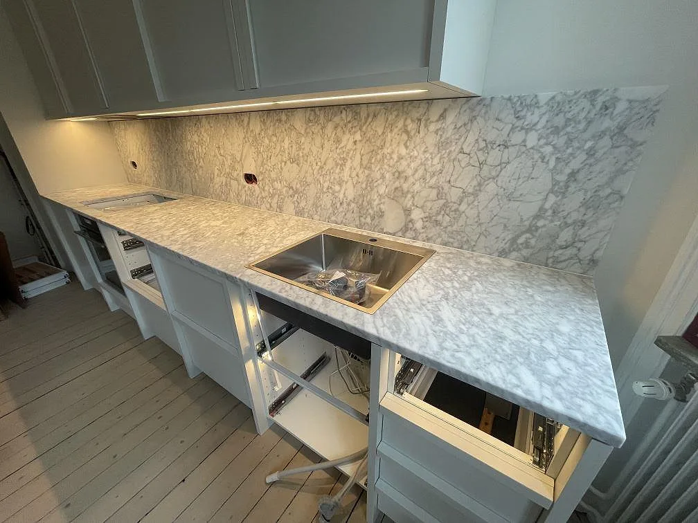 Matt köksbänkskiva i Carrara C marmor med rostfri diskho, öppen köksstomme och tydlig grå ådring i Stockholm.