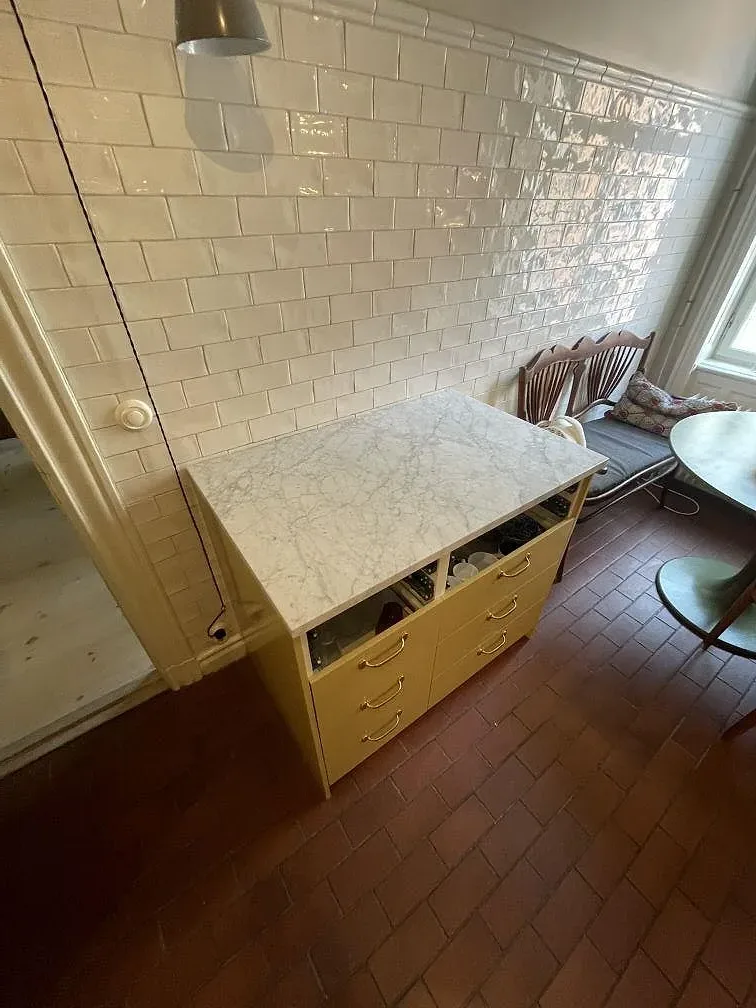 Måttanpassad bänkskiva i Carrara C marmor på en gul förvaringsmöbel i Stockholm.