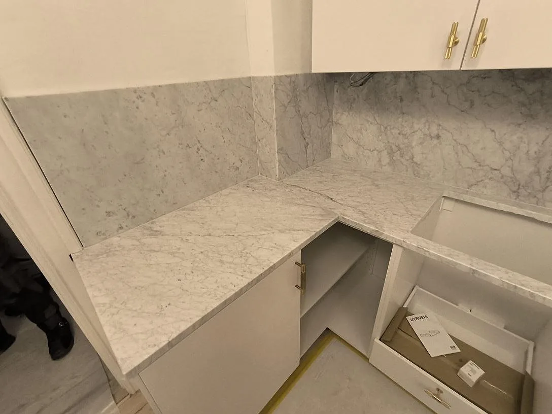 Närbild på L-hörn i polerad Carrara C marmor med ådring, stänkskydd och öppen köksstomme i Stockholm.
