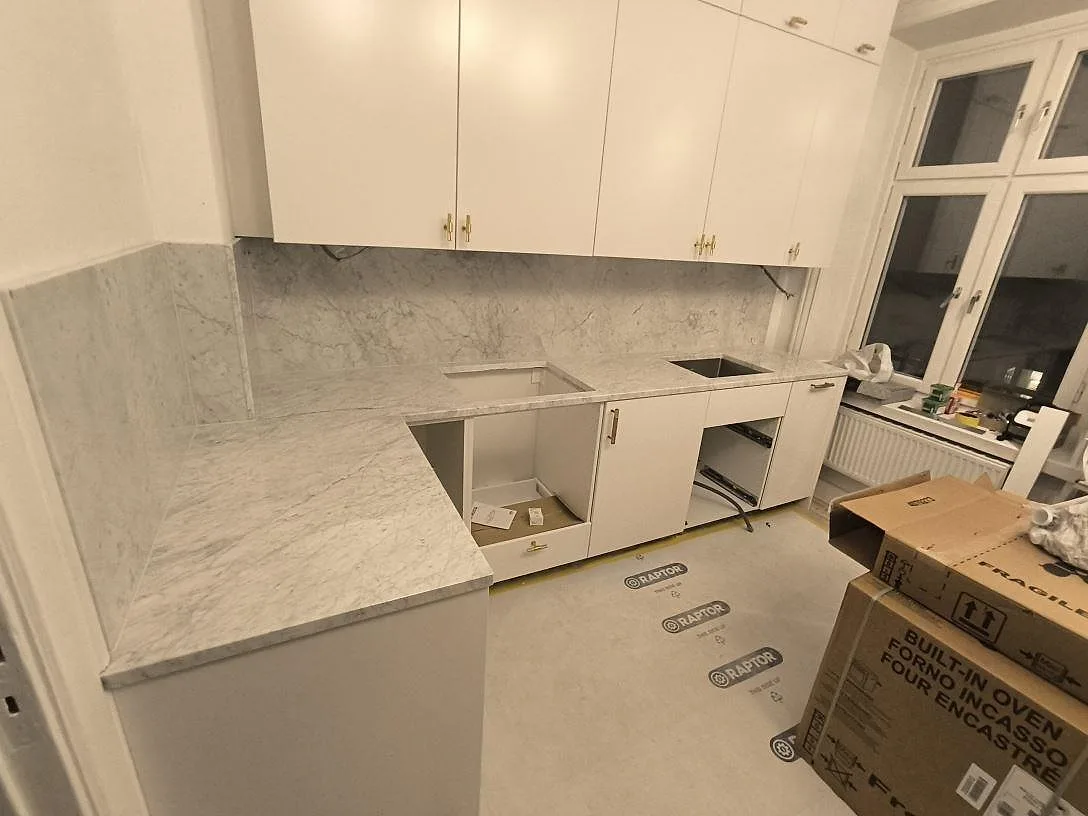 Polerad marmorbänkskiva i Carrara C med öppningar i arbetsytan och högt stänkskydd i ett kök under montering i Stockholm.