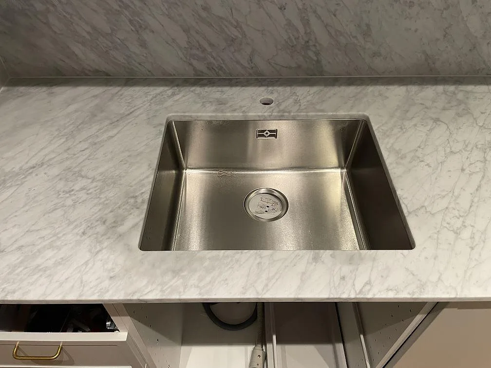 Närbild på matt Carrara C marmor med rostfri diskho och grå ådring i ett kök i Stockholm.