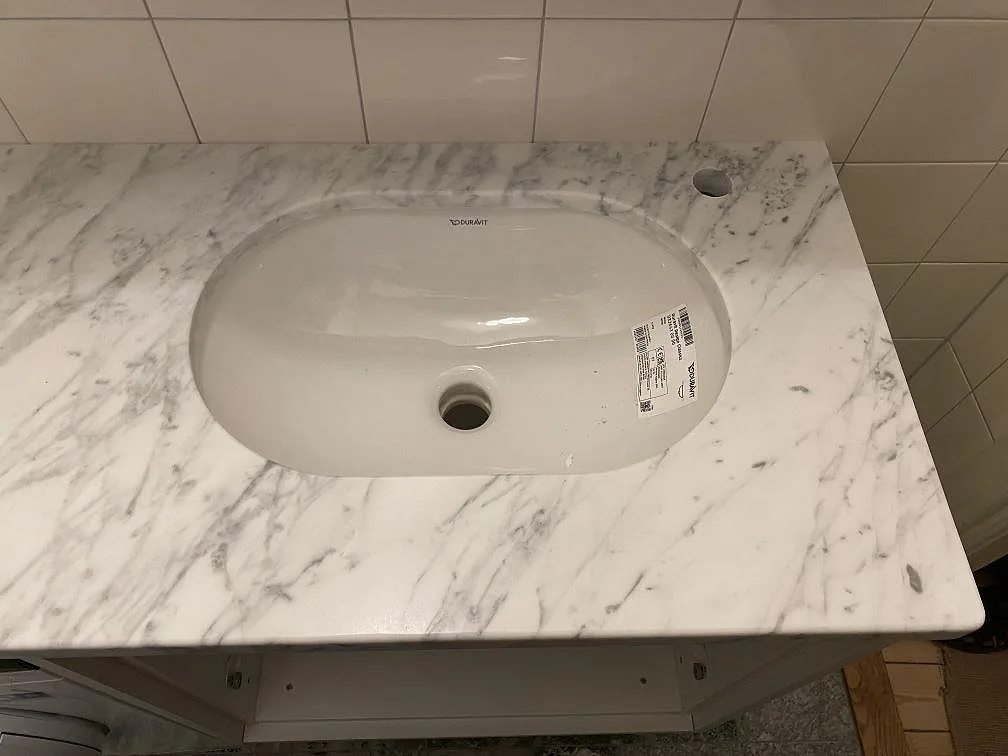 Närbild på det underlimmade ovala Duravit-handfatet i porslin i den matta Carrara C-marmorskivan i ett badrum i Stockholm, med ett separat hål för blandaren.
