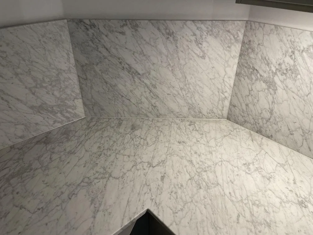 Närbild på den grå ådringen i Carrara C marmor där bänkskiva och stänkvägg möts i ett hörn i ett kök i Stockholm.