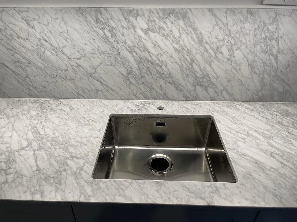 Underlimmad rostfri diskho i en matt köksbänkskiva av Carrara C marmor med tydlig grå ådring i ett kök i Stockholm.