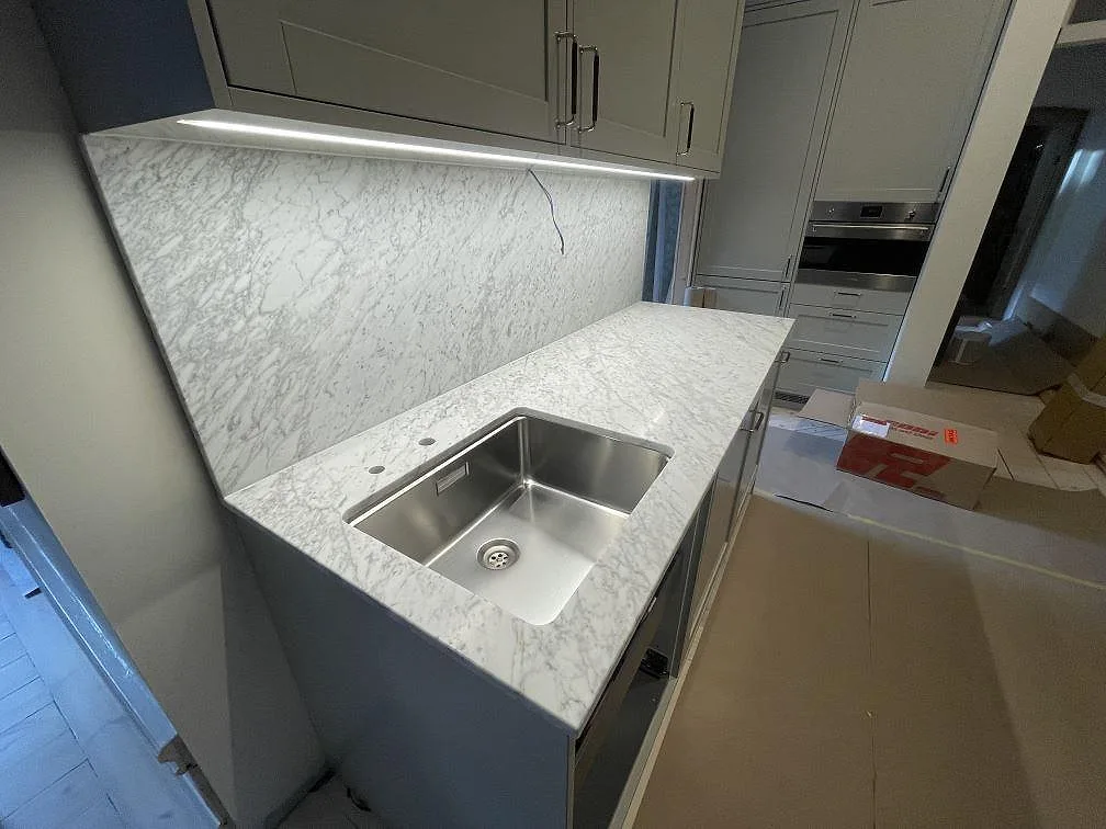 Matt Carrara C-marmor med diagonal grå ådring och underlimmad rostfri diskho längs en köksbänk med marmorstänkvägg i Stockholm.